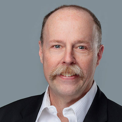 Brent Neville headshot. He has short hair and a greying moustache and he's smiling.